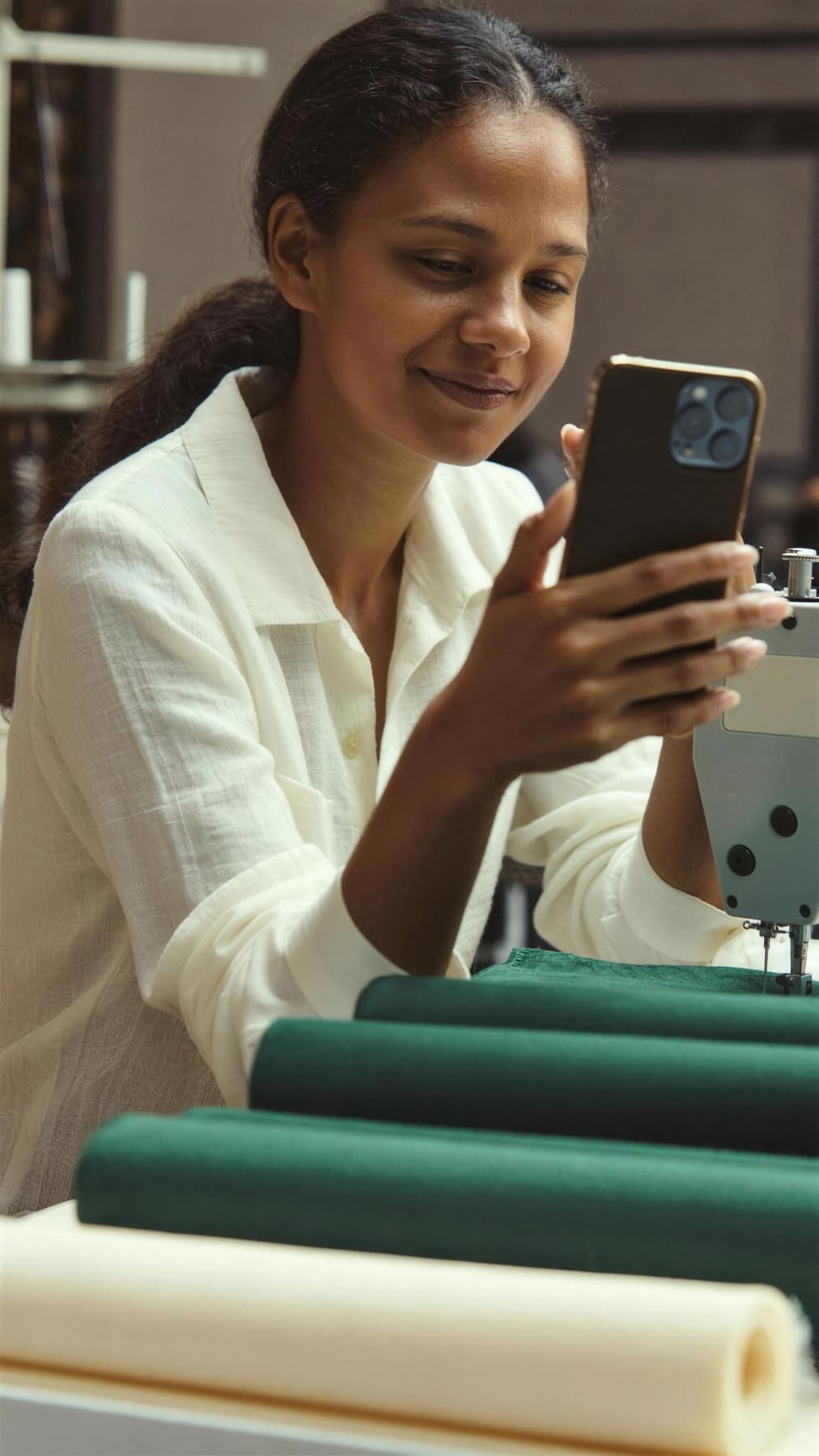 Costureira de confecção sorrindo para o celular na oficina